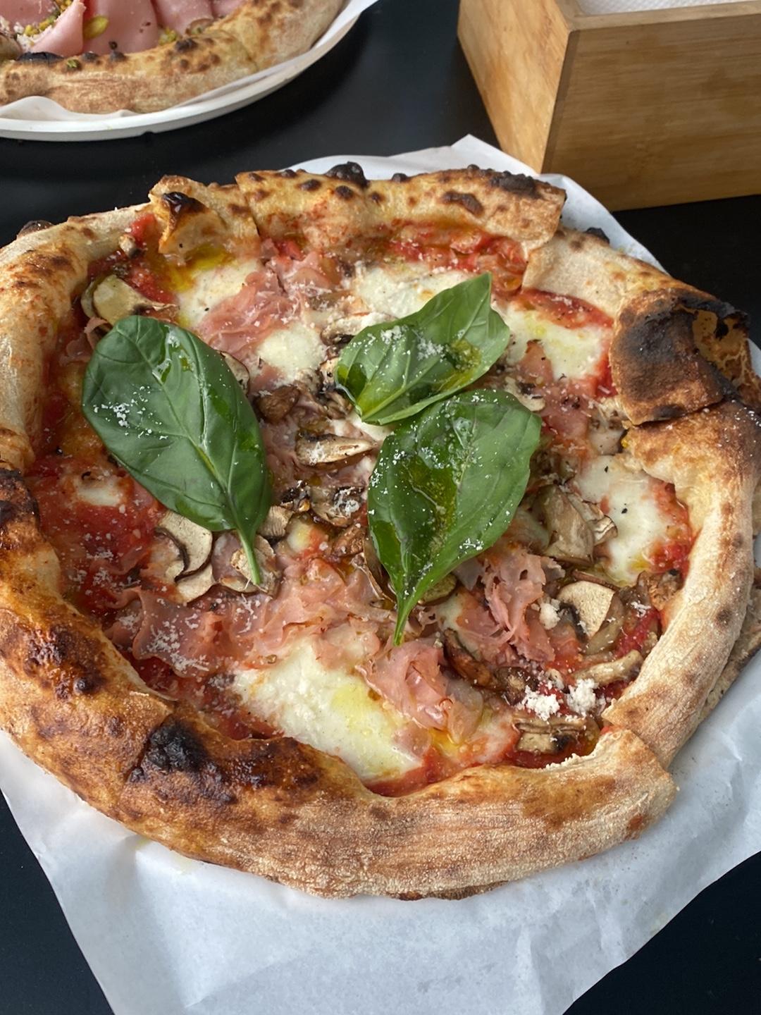 Pizza cu marginea umflată și arsă pe alocuri, cu prosciutto și busuioc